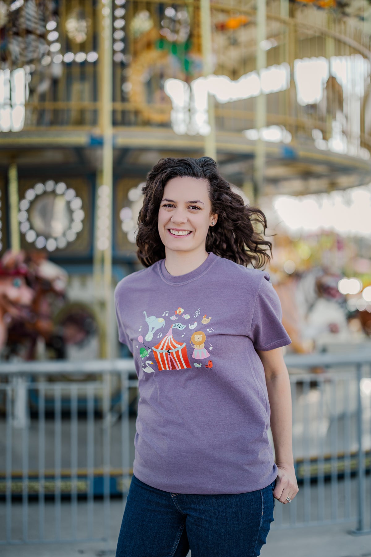 Person wearing a purple t-shirt with a colorful design in front of a carousel.