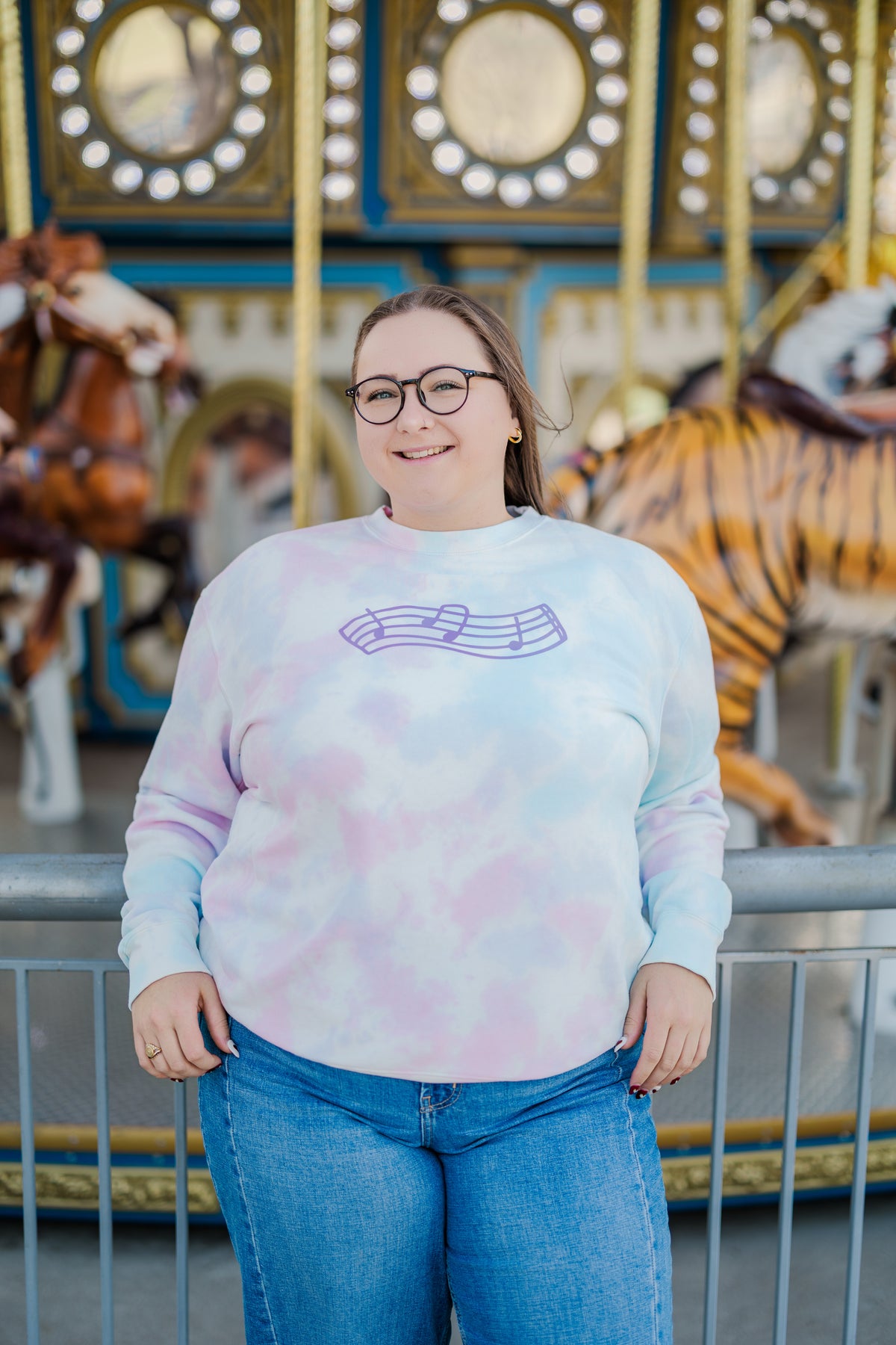 Person wearing a tie-dye sweatshirt with a graphic design in front of a carousel.
