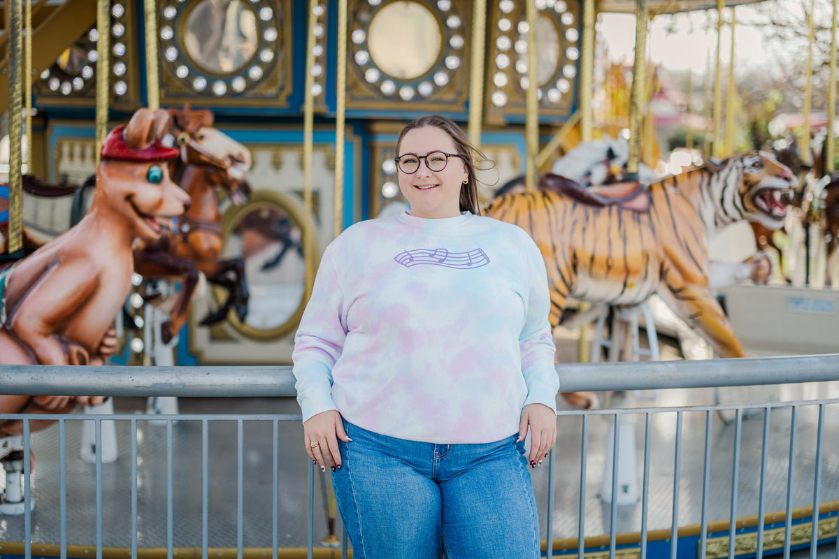 Person wearing a tie-dye sweatshirt in front of a carousel with colorful horses.