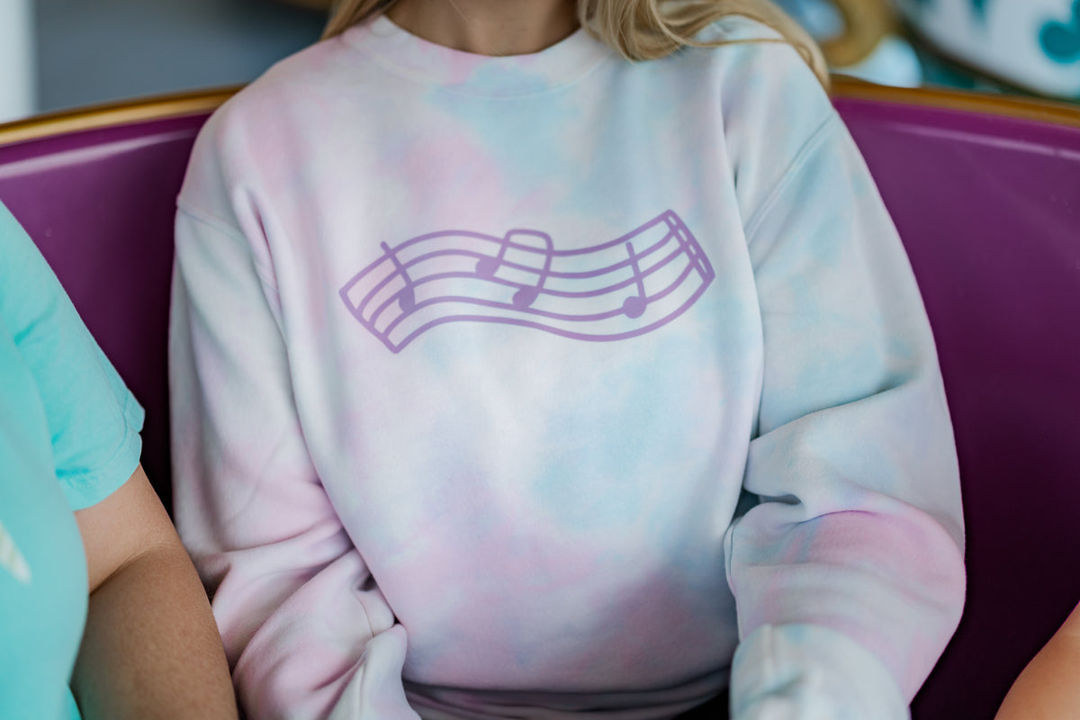 Person wearing a tie-dye sweatshirt with a music note design on a purple ride at a carnival.