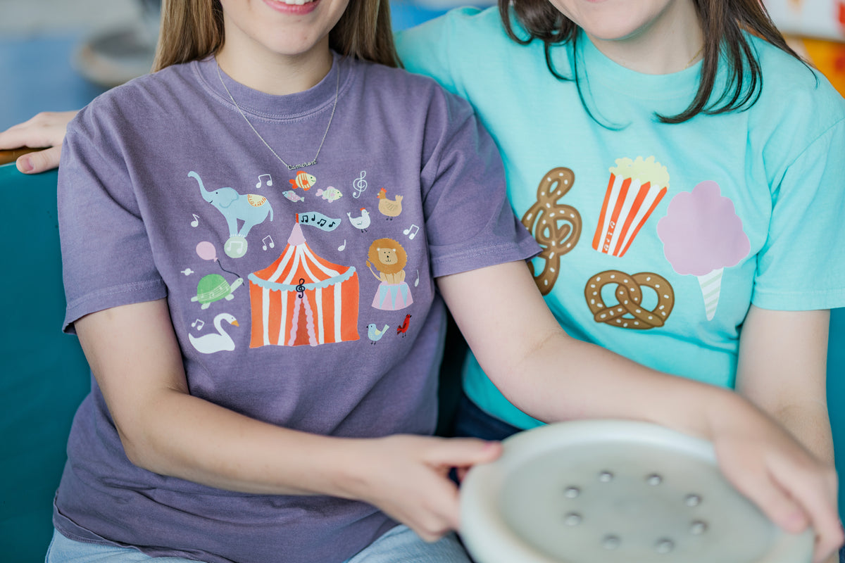 Two women wearing colorful t-shirts with cartoon designs, sitting together.