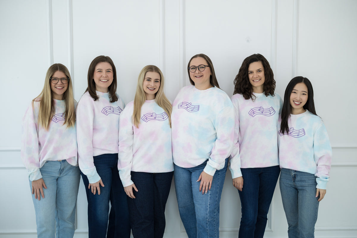 Group of six women wearing tie-dye sweatshirts with a logo against a white background