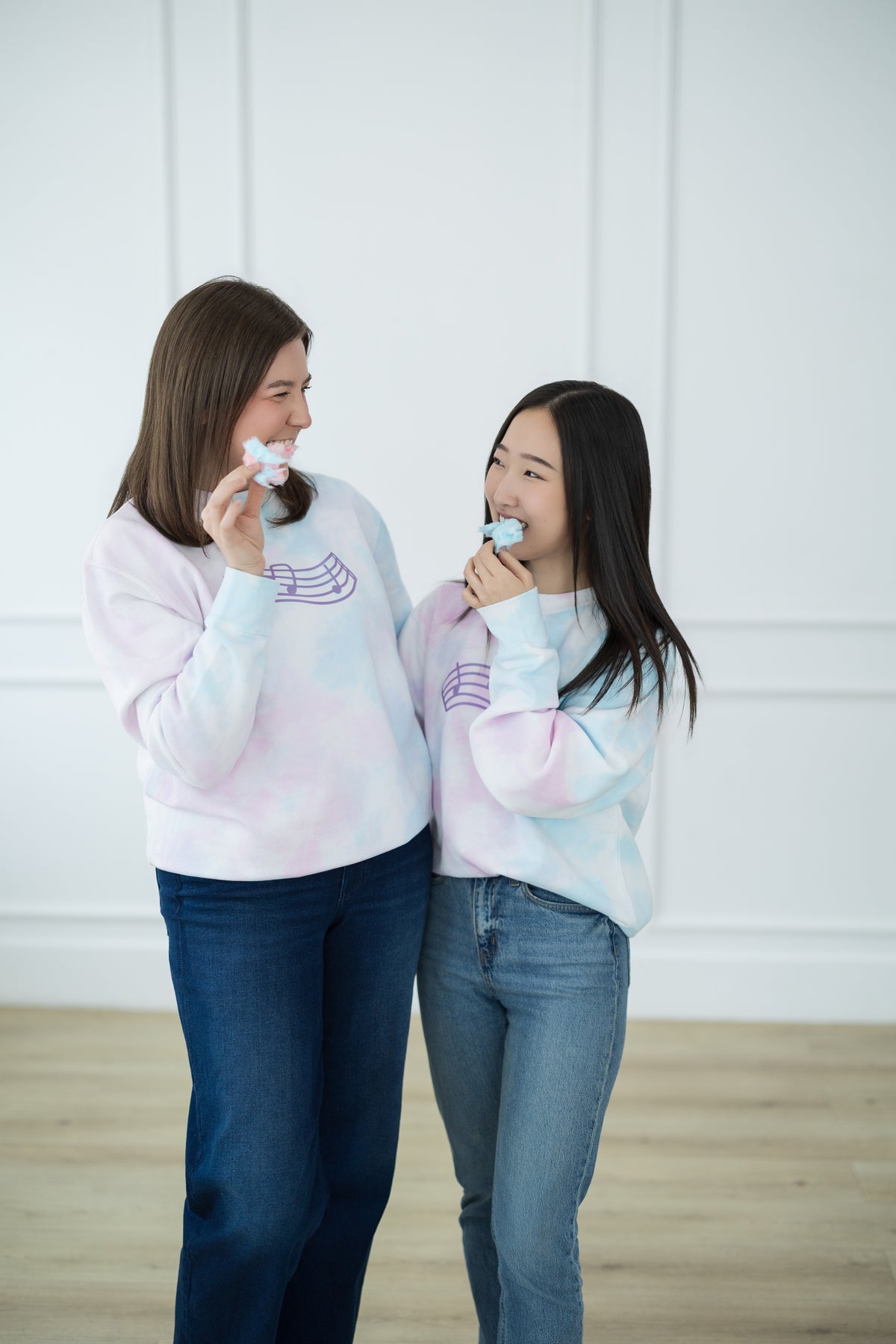 Two women wearing matching sweatshirts and jeans against a white background