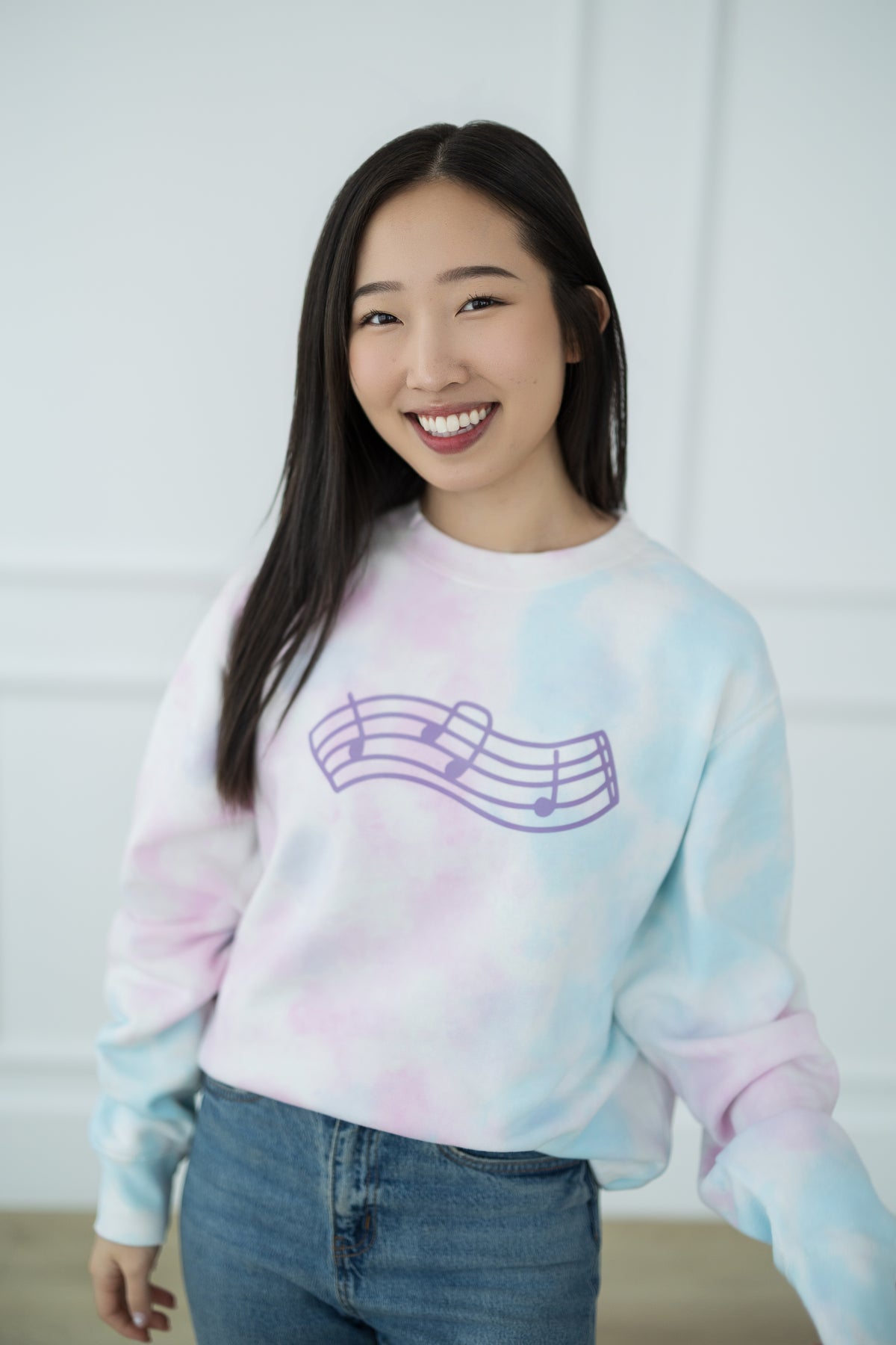 Person wearing a tie-dye sweatshirt with a music note design against a white background