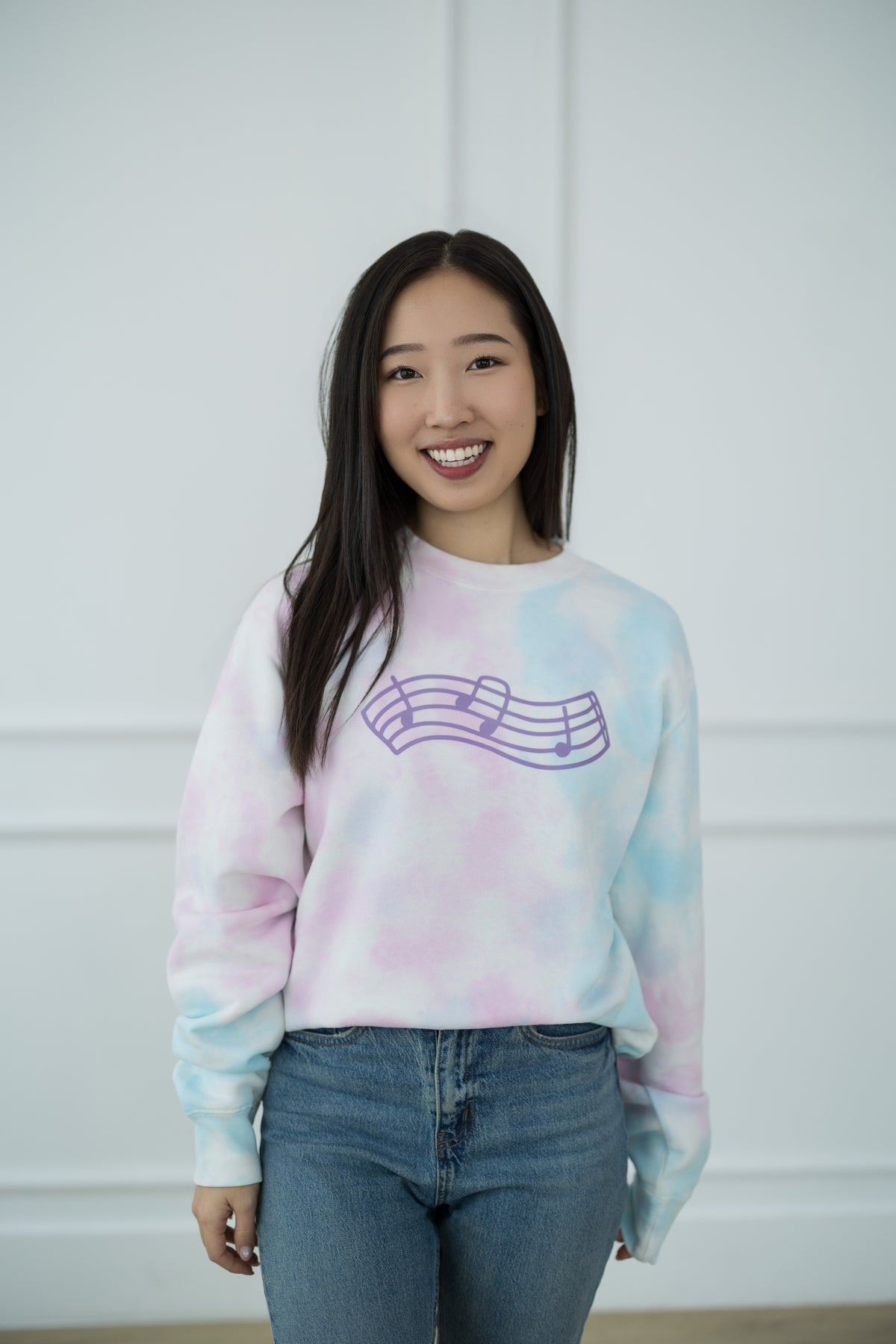 Person wearing a tie-dye sweatshirt with a graphic design against a plain background