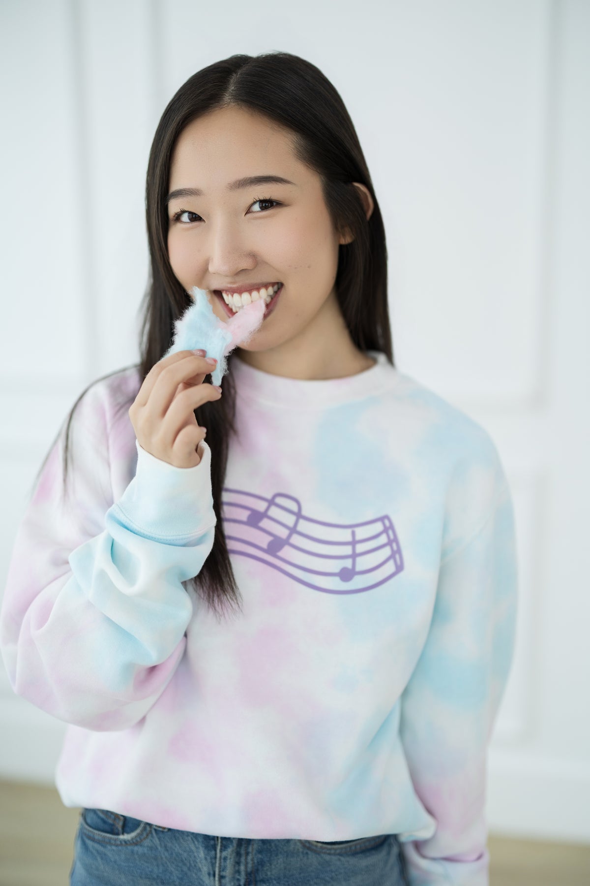 Person wearing a pastel tie-dye sweater with a music note design, holding a cotton candy.