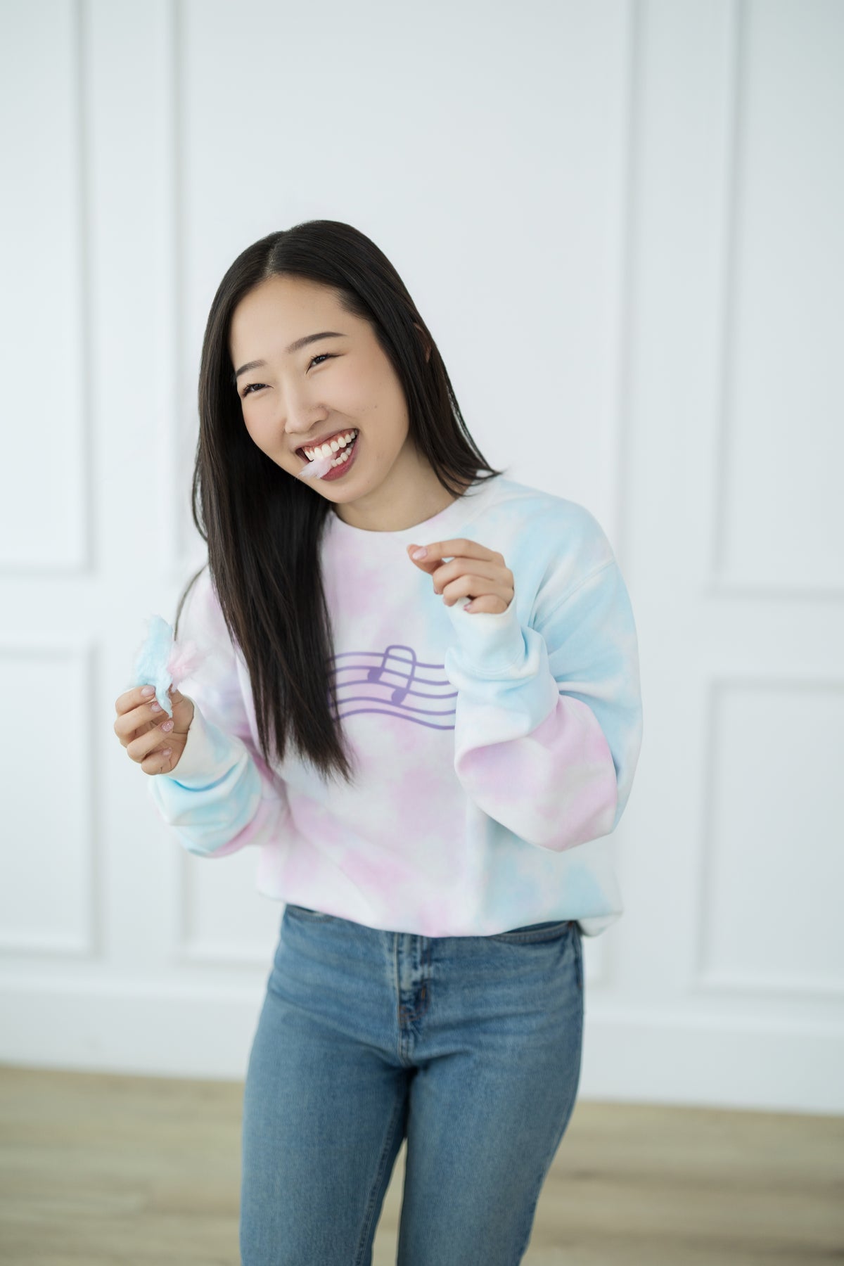 Woman wearing a tie-dye sweater and jeans against a white wall