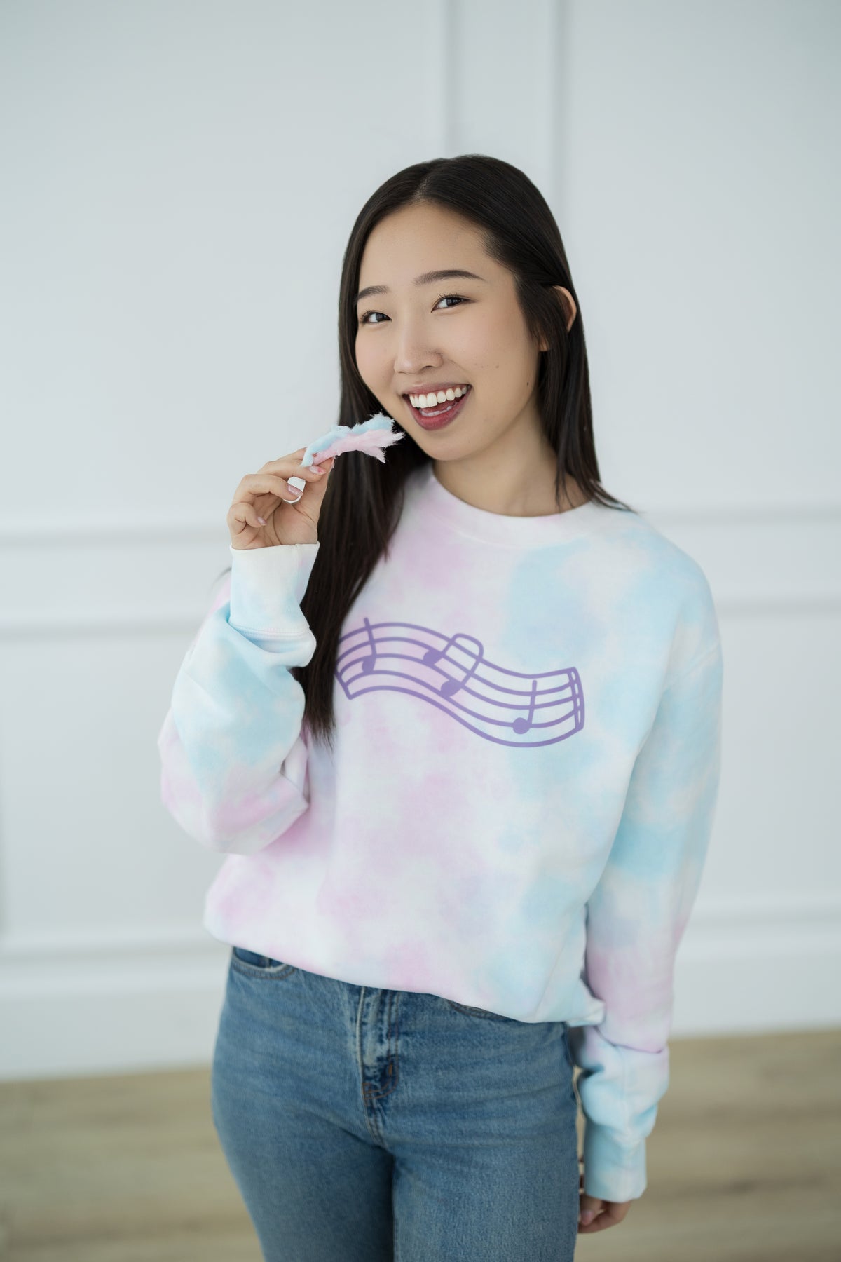 Woman wearing a tie-dye sweatshirt with a music note design, holding cotton candy.