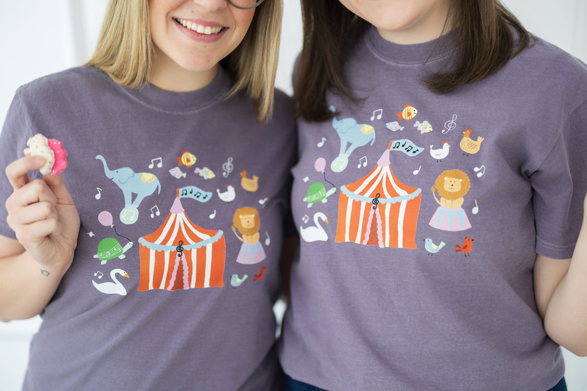 Two people wearing purple t-shirts with colorful carnival-themed designs.