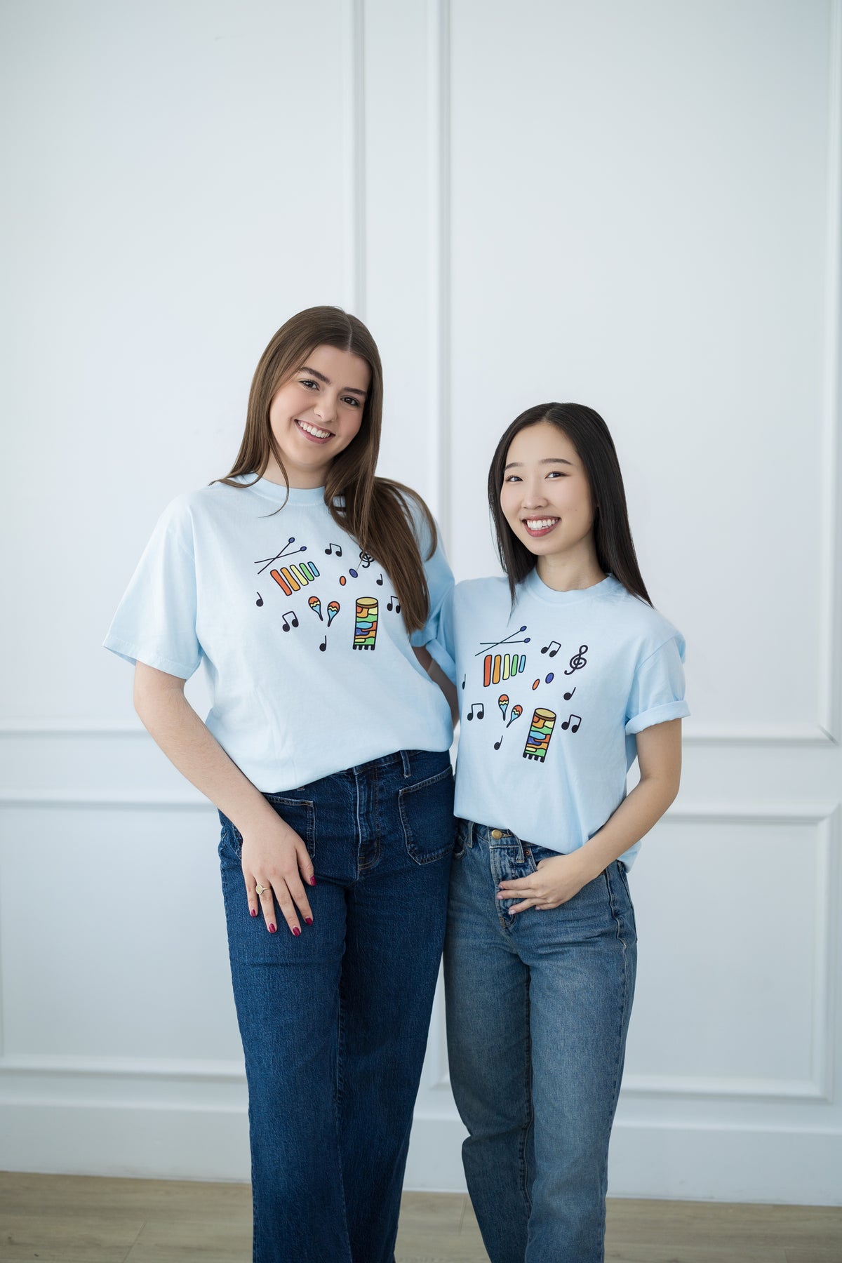 Two women wearing matching light blue t-shirts with colorful designs against a white background