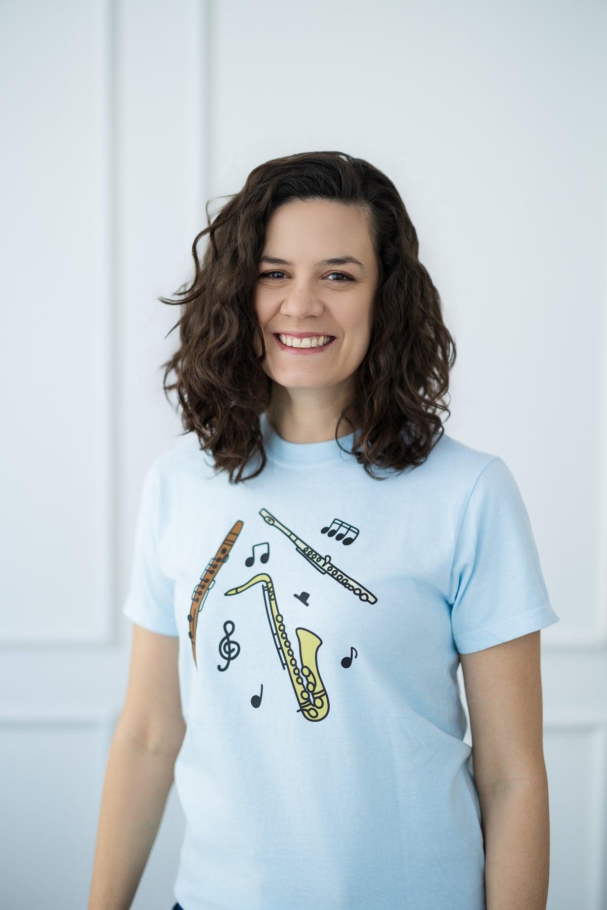 Woman wearing a light blue t-shirt with musical instrument designs on a white background