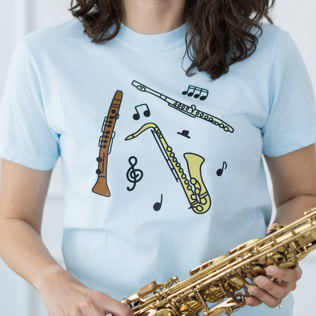 Person holding a saxophone wearing a light blue t-shirt with musical designs.