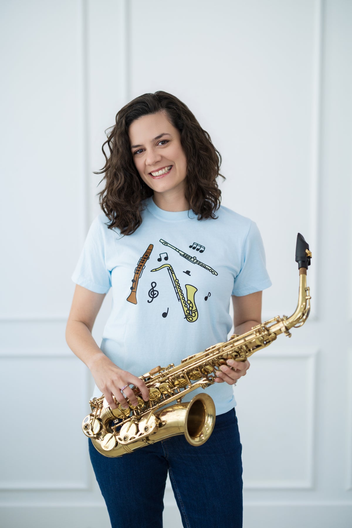 Person holding a saxophone wearing a light blue t-shirt with musical instrument designs against a white background