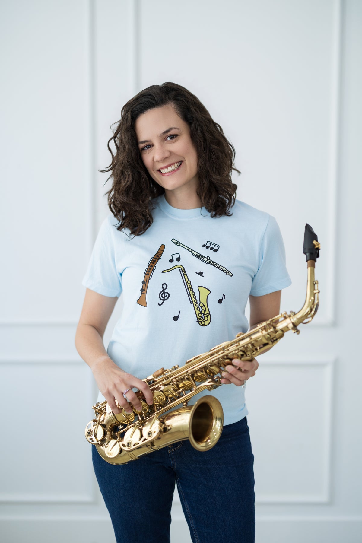 Woman holding a saxophone wearing a light blue t-shirt with musical instrument designs.