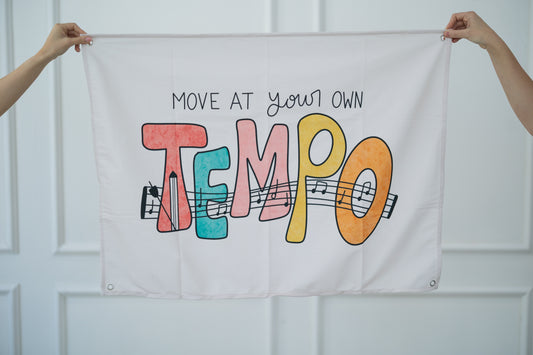 Person holding a tapestry with 'Move at your own tempo' text and colorful letters against a white background