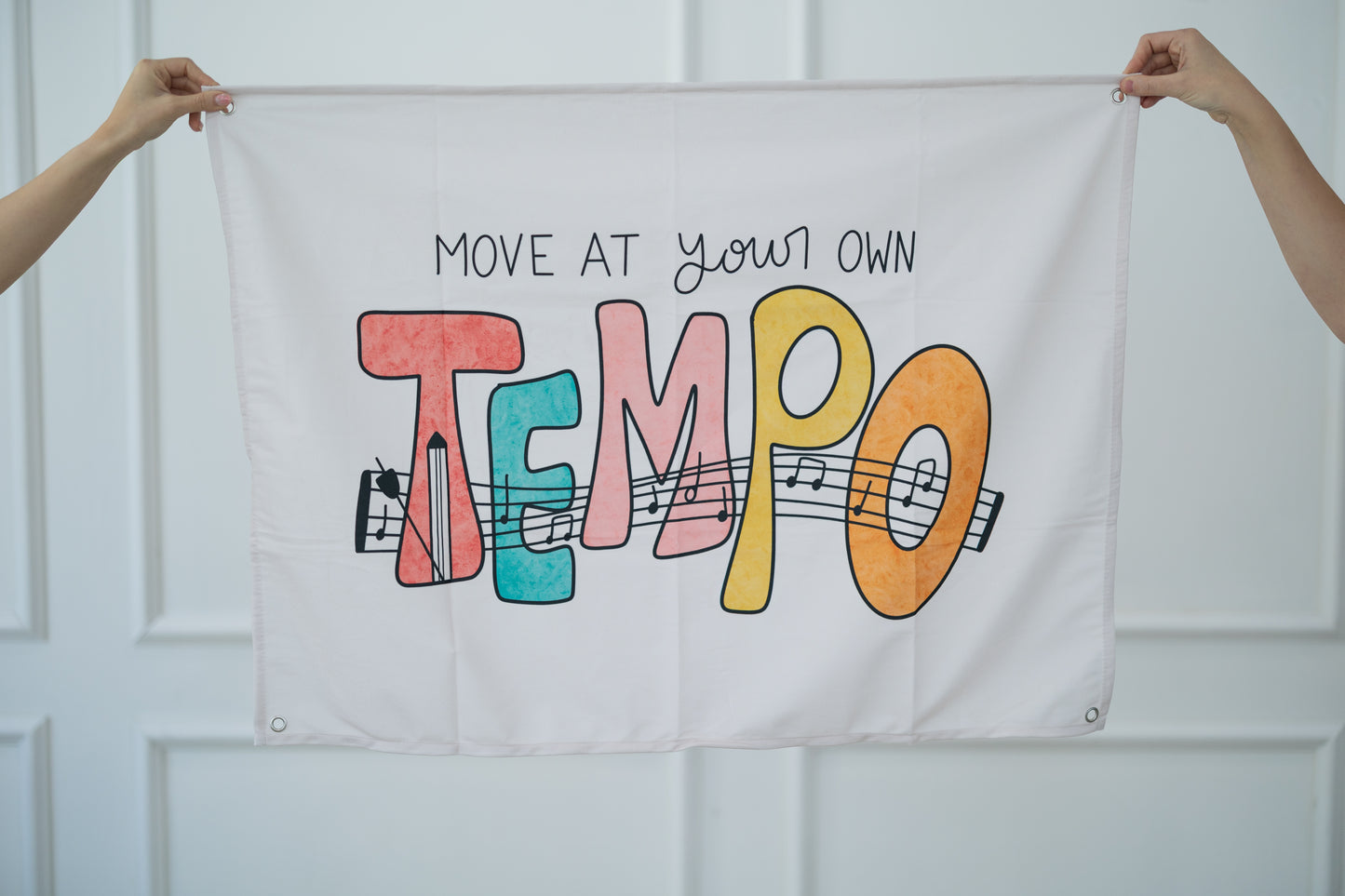 Person holding a tapestry with 'Move at your own tempo' text and colorful letters against a white background
