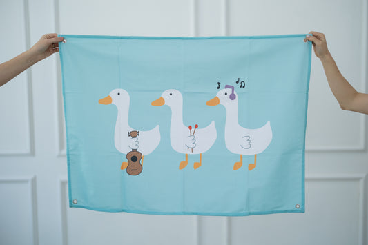 Teal tapestry with cartoon geese held by two hands against a white background