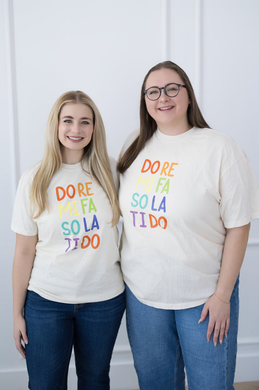 Two people wearing matching white t-shirts with colorful text on a plain background