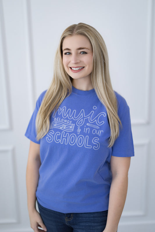 Person wearing a blue t-shirt with 'Music Belongs in Our Schools' text against a white background