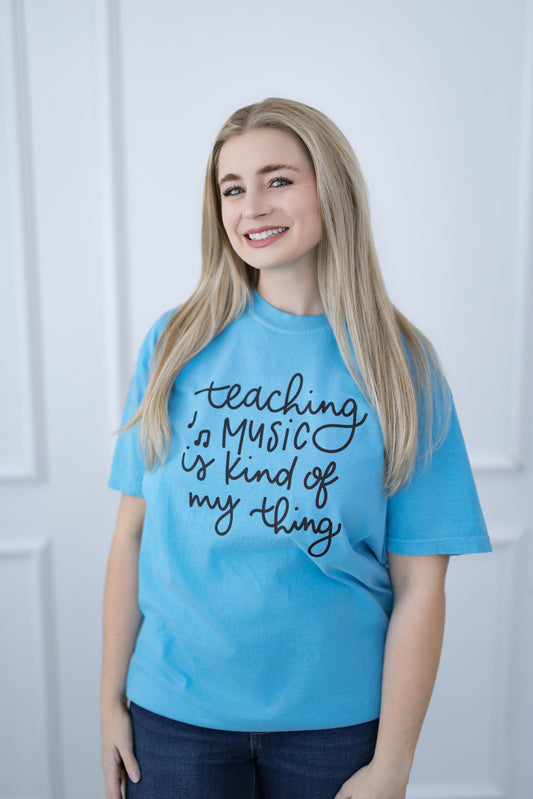 Woman wearing a blue t-shirt with 'teaching is music is kind of my thing' text.
