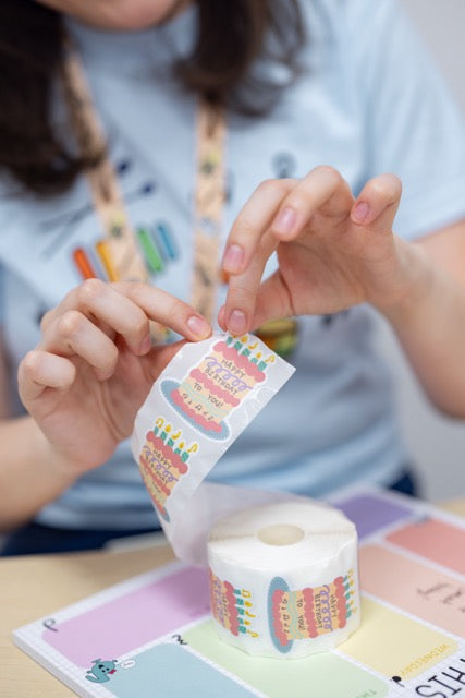 Person holding a roll of colorful stickers with a lanyard around their neck.