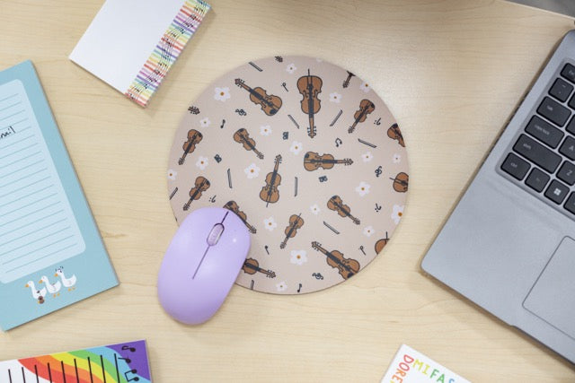 Round mouse pad with violin pattern on a desk with laptop, mouse, and stationery.