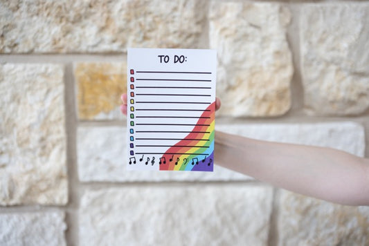 Hand holding a colorful 'To Do' list with a rainbow design against a stone wall background
