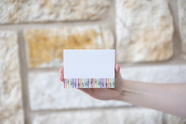 Hand holding white sticky notes with colorful music inspired pattern against a textured wall.