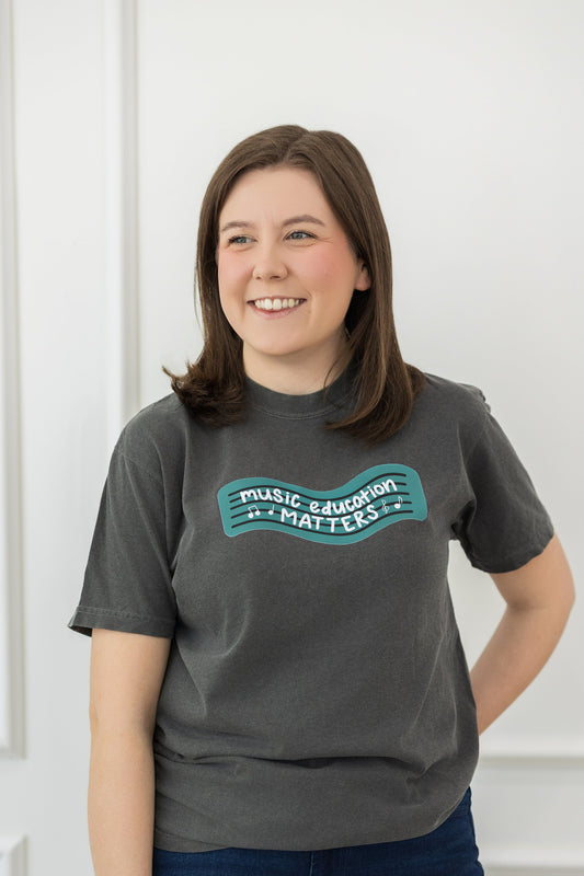 Person wearing a gray t-shirt with text, standing against a white door.