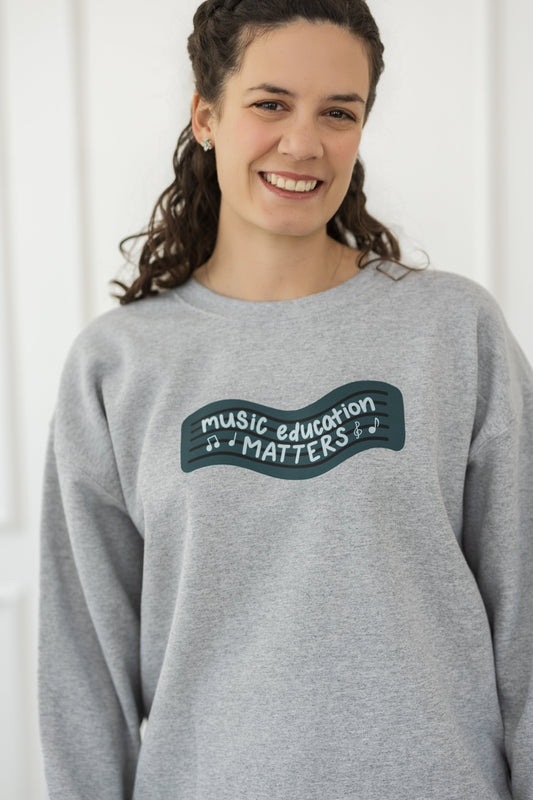 Person wearing a gray sweatshirt with 'Music Education Matters' text on a white background