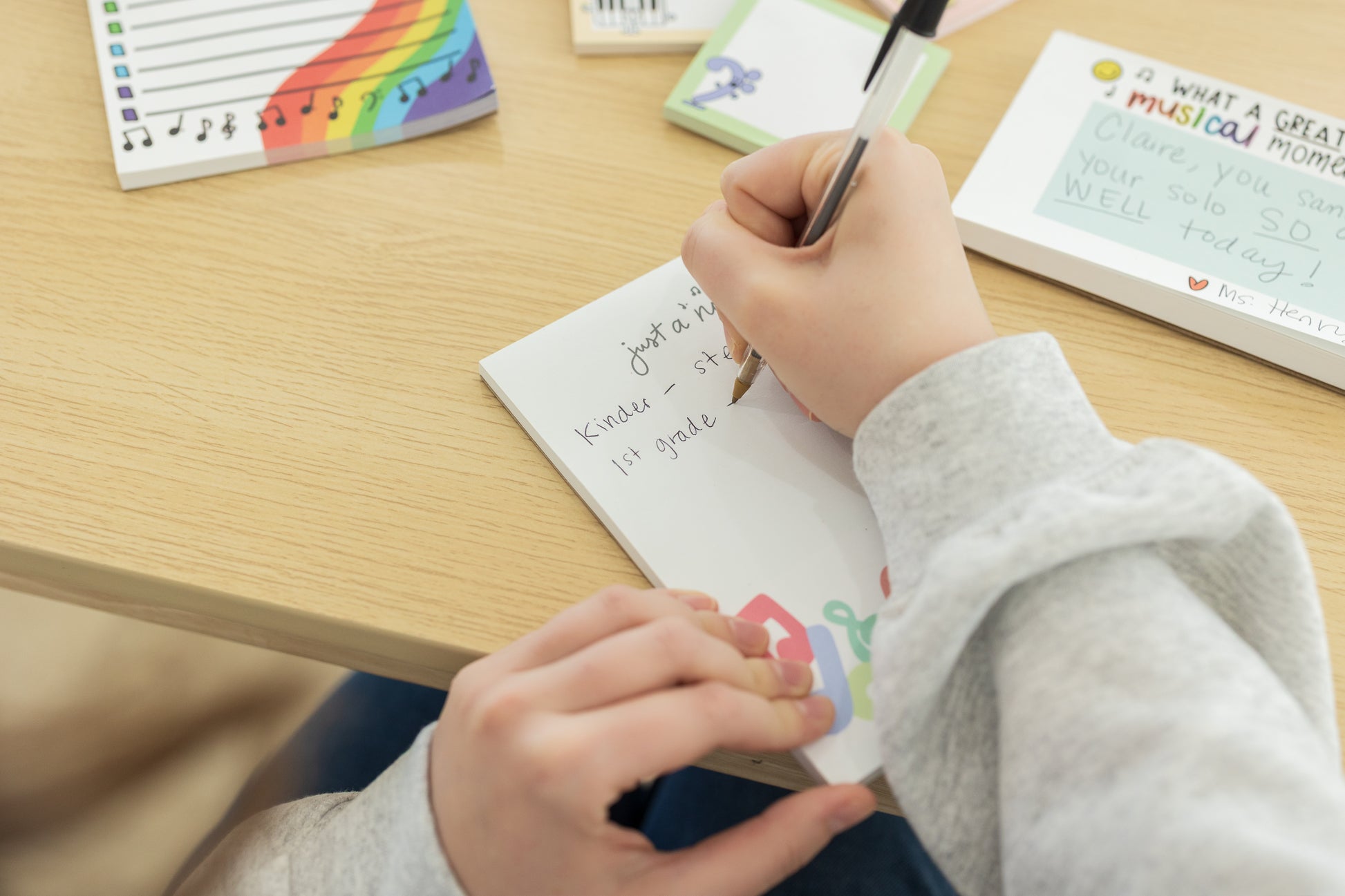 Person writing in a notebook with colorful stationery items on a desk