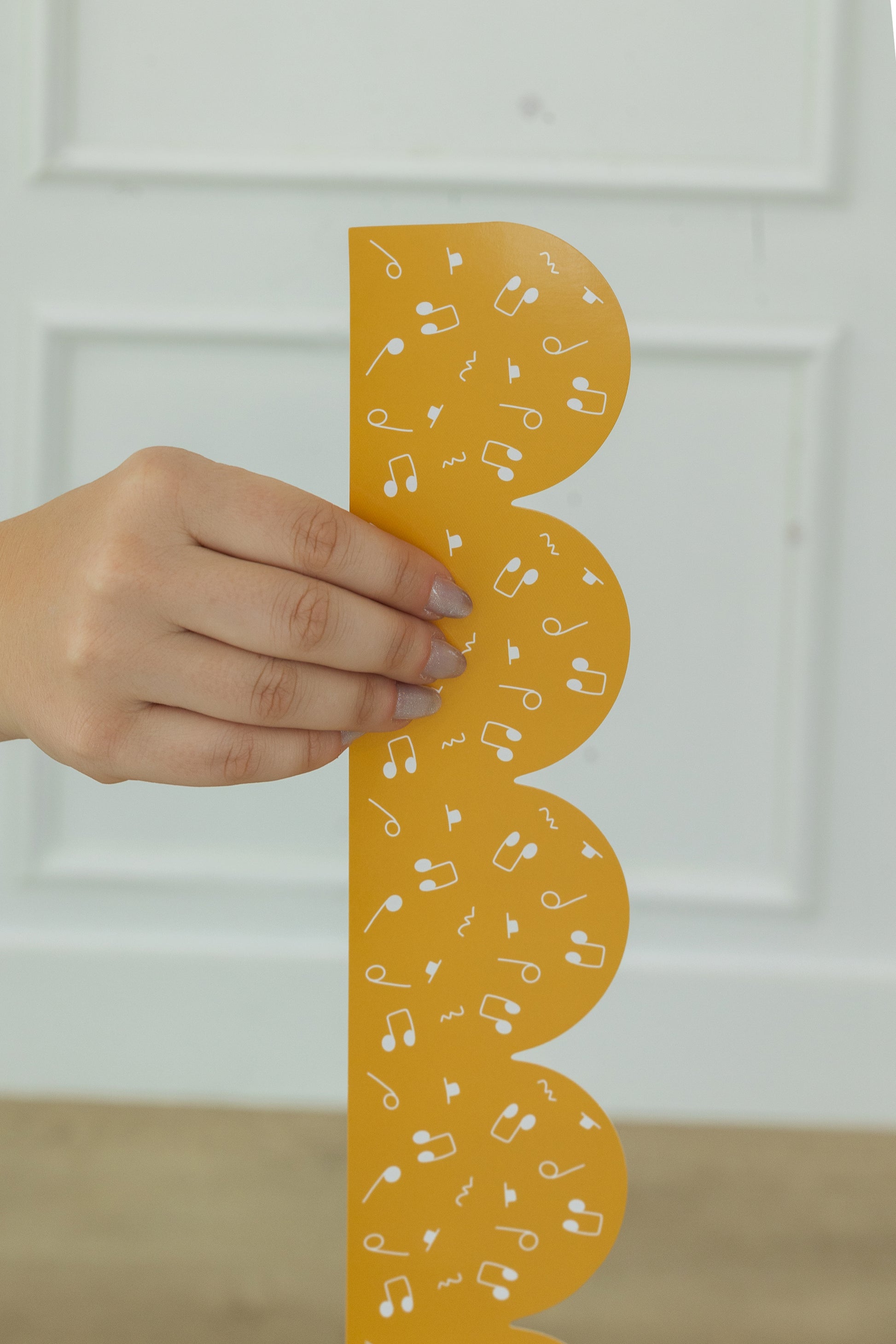Hand holding a yellow bulletin board border with musical notes against a white background