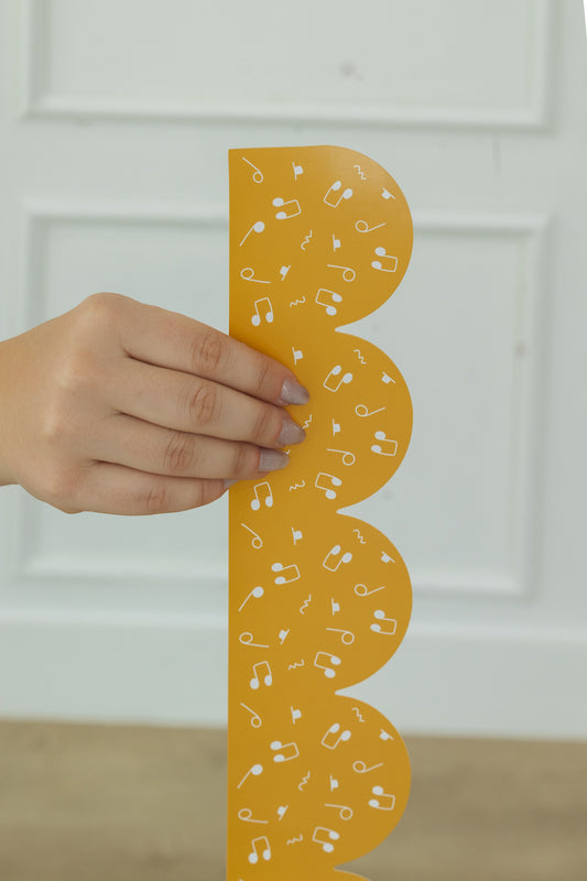 Hand holding a yellow bulletin board border with musical notes against a white background