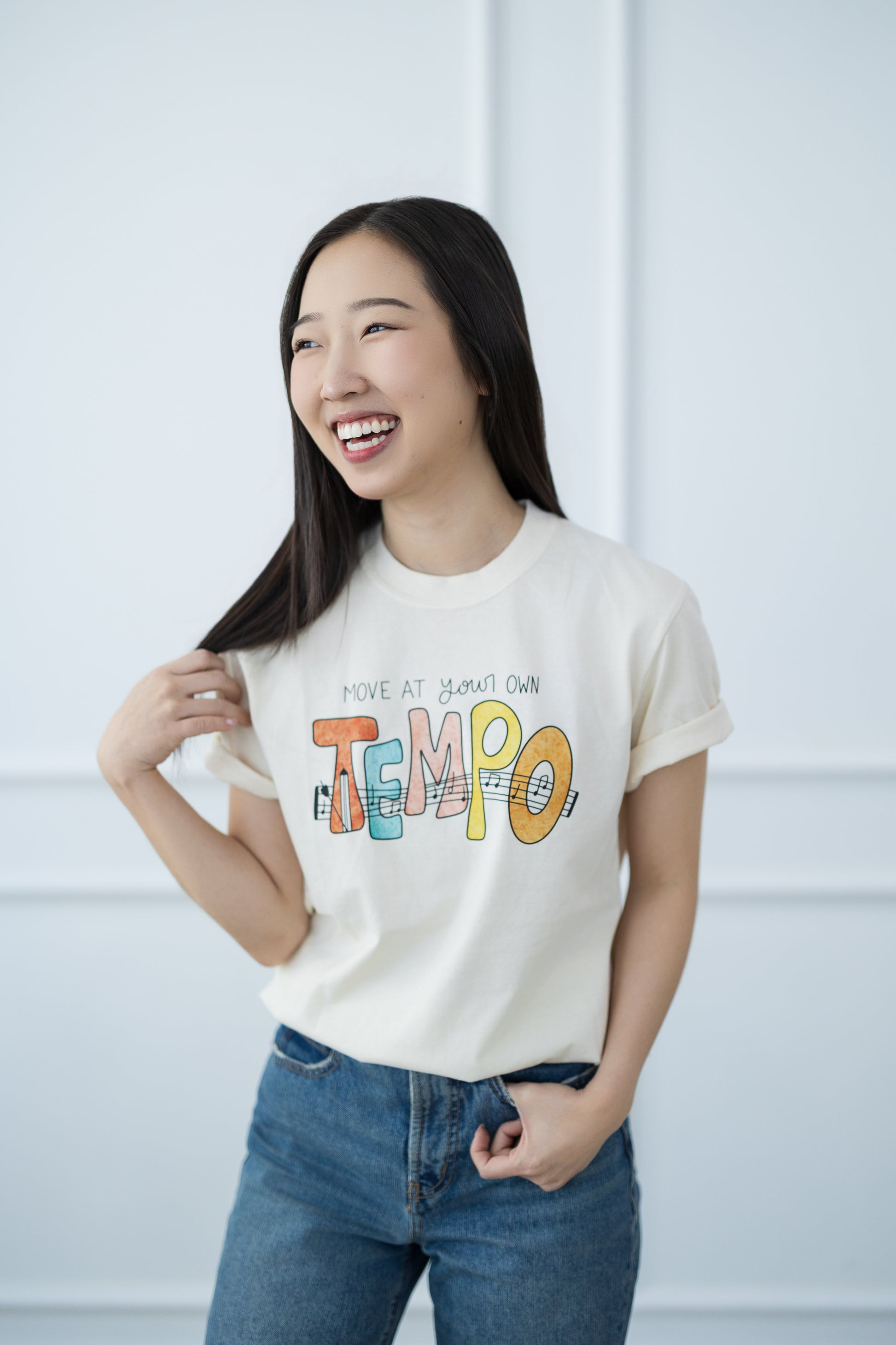 Woman wearing a white t-shirt with colorful text and blue jeans against a light background
