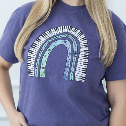 Woman wearing a purple t-shirt with a colorful design against a white paneled wall.