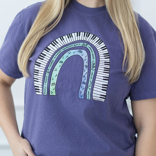 Woman wearing a purple t-shirt with a colorful design against a white paneled wall.