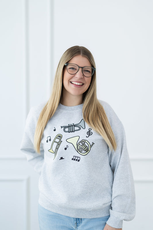 Woman wearing a gray sweatshirt with musical instrument designs against a white wall.