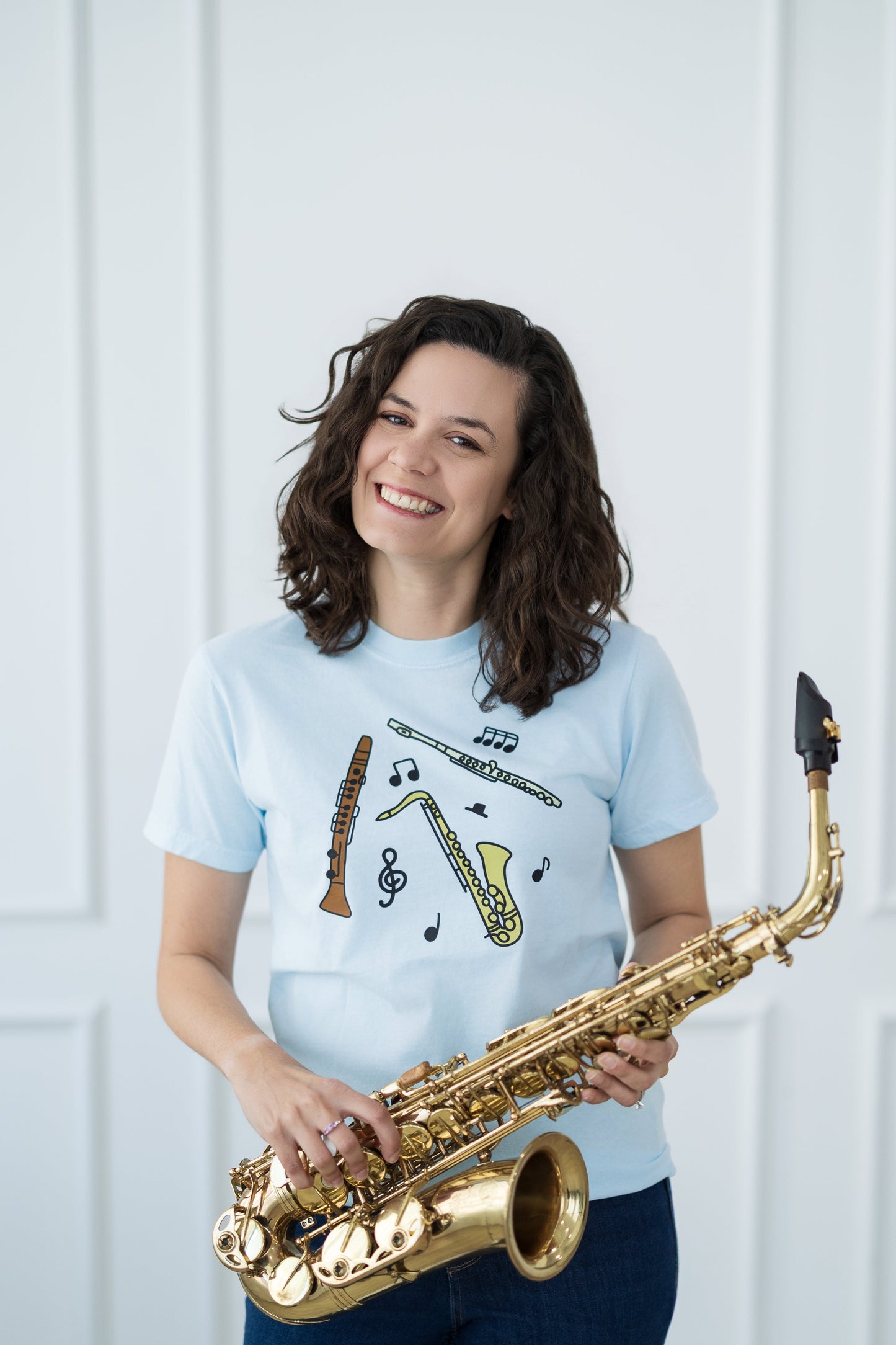 Person holding a saxophone wearing a light blue t-shirt with musical designs.