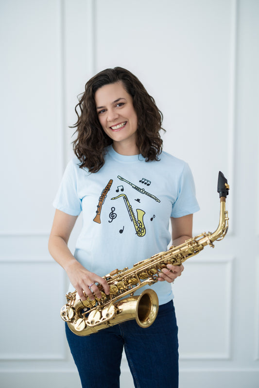 Person holding a saxophone wearing a light blue t-shirt with musical instrument designs against a white background