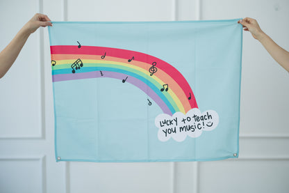 Tapestry with a rainbow and musical notes design held by two hands against a white background