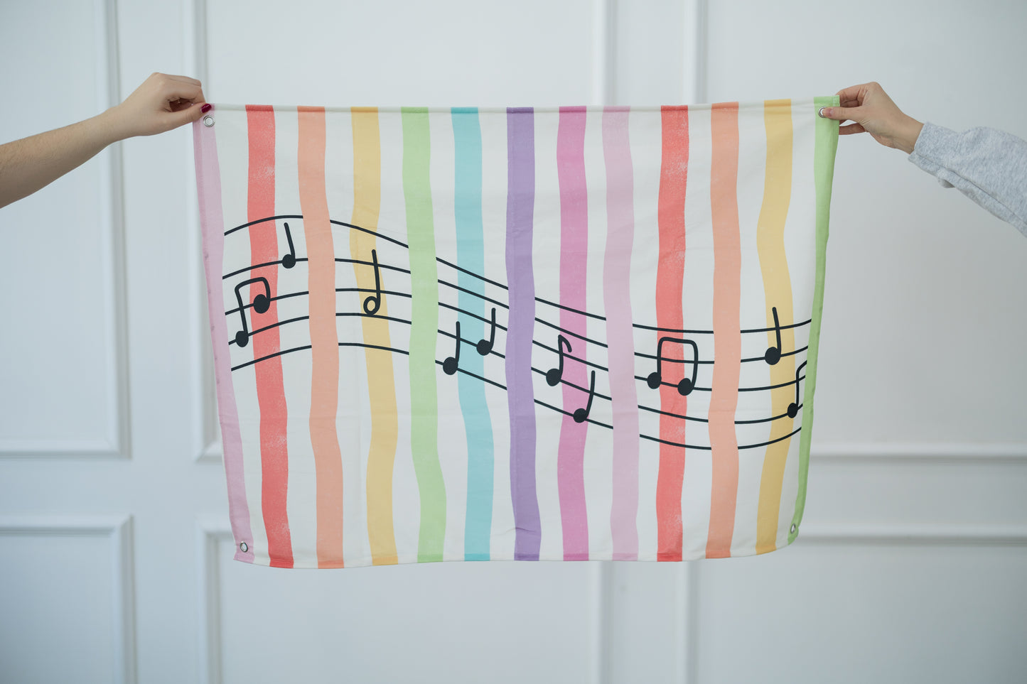 Colorful tapestry with musical notes held by two hands against a white background