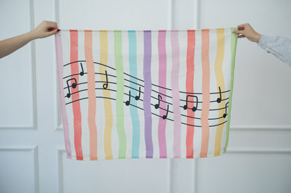 Colorful tapestry with musical notes held by two hands against a white background