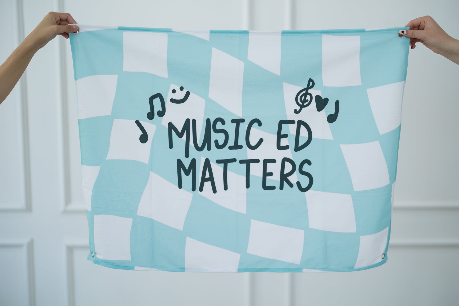 Checkered tapestry with 'Music Ed Matters' text held by two hands against a white background