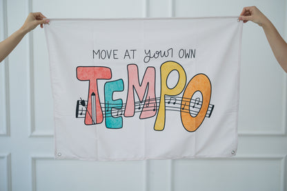 Person holding a tapestry with 'Move at your own tempo' text and colorful letters against a white background