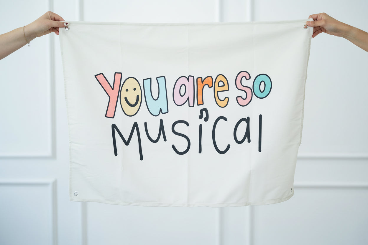 Textile with 'You are so musical' printed on it held by two hands against a white background
