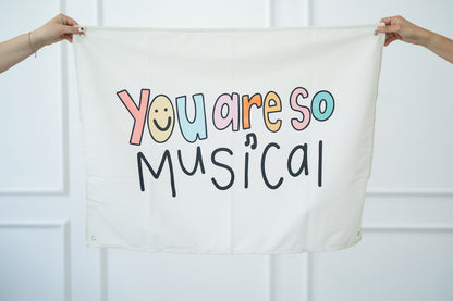 Textile with 'You are so musical' printed on it held by two hands against a white background
