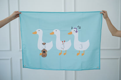 Teal tapestry with cartoon geese held by two hands against a white background