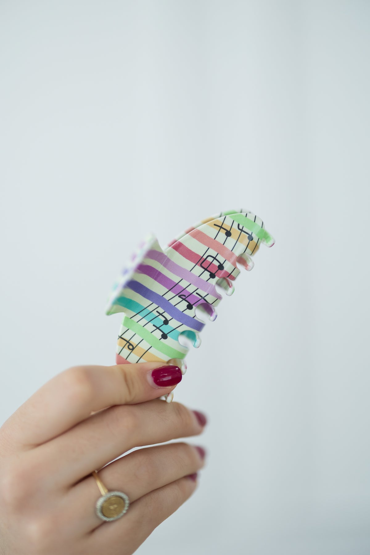 Hand holding a colorful music note hair clip against a light gray background