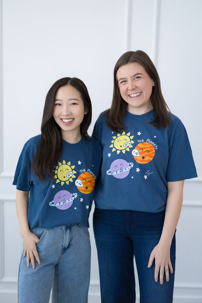 Two people wearing blue t-shirts with space-themed designs against a white background