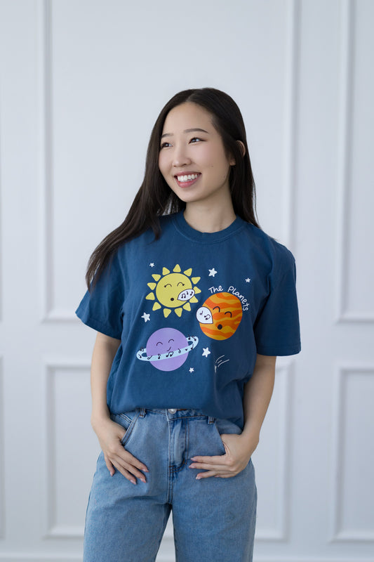 Woman wearing a blue t-shirt with space-themed graphics against a white paneled wall.